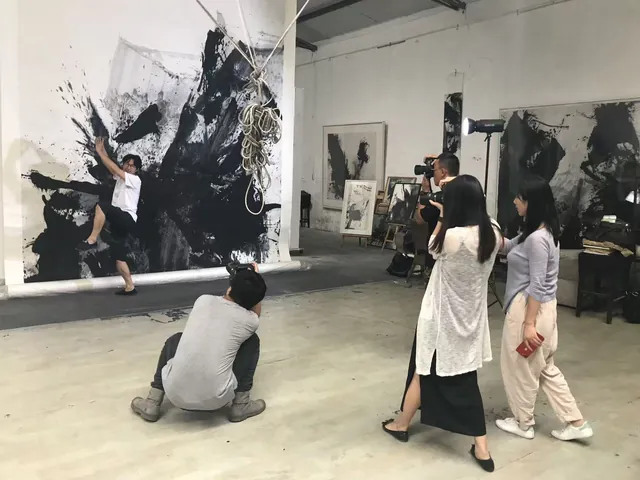 工作室中人物在画作前摆姿势，摄影者与观看者在场