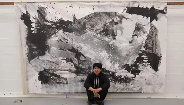 人物蹲坐于工作室大型水墨作品前